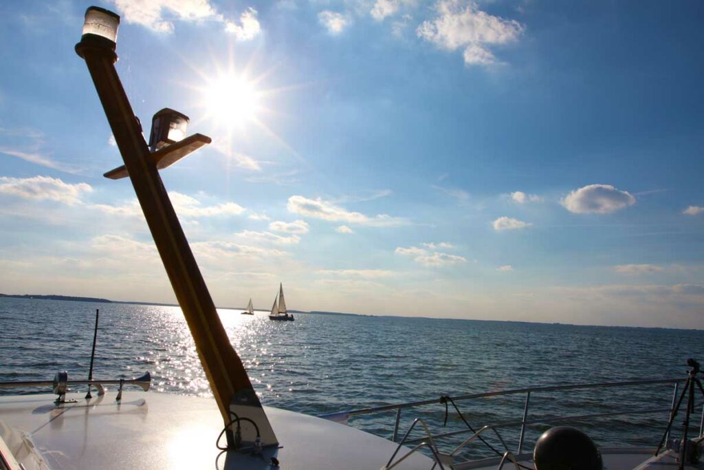 Ein Motorboot quert die Müritz bei strahlendem Sonnenschein und Segelbooten im Hintergrund.