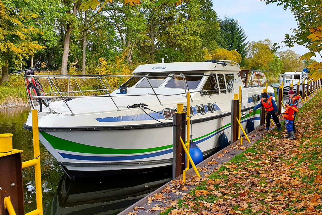Hausboot liegt vor einer Schleuse im Herbst und Kindern in der Mecklenburgischen Seenplatte